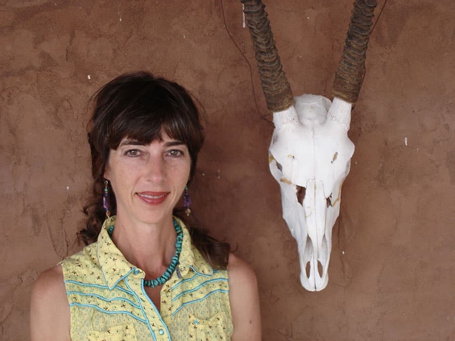 Dr. Gayle MacKenzie in a yellow western shirt and turquoise necklace, against an adobe wall