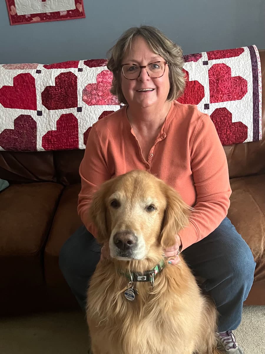 Nicki McIntosh at home on a leather couch with her golden retriever, Bear